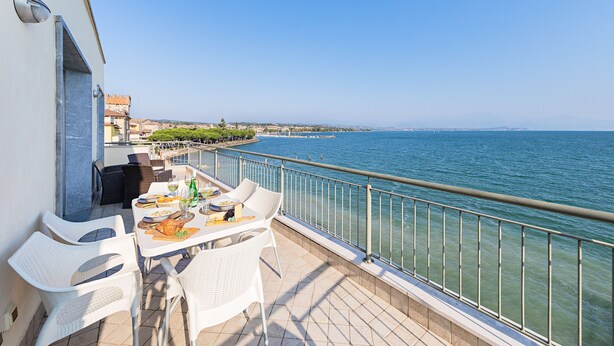 A balcony with a dining table and chairs overlooking a body of water. - Residenza Miralago - 20 Porzia - Locazione BK (Desenzano del Garda)