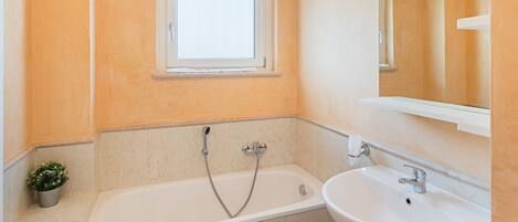 A bathroom with a bathtub, a sink, and a window.