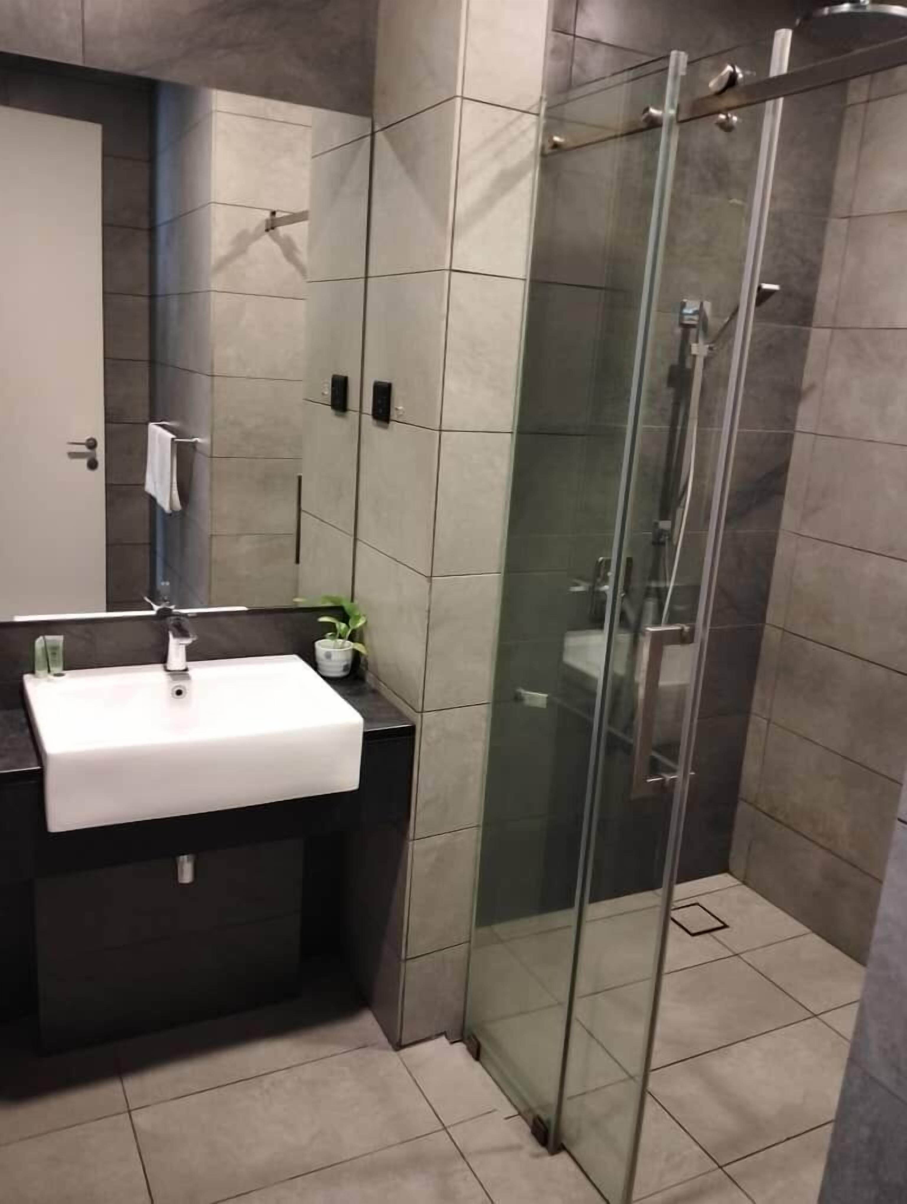 A modern bathroom with a white sink, dark countertop, and a glass shower enclosure.