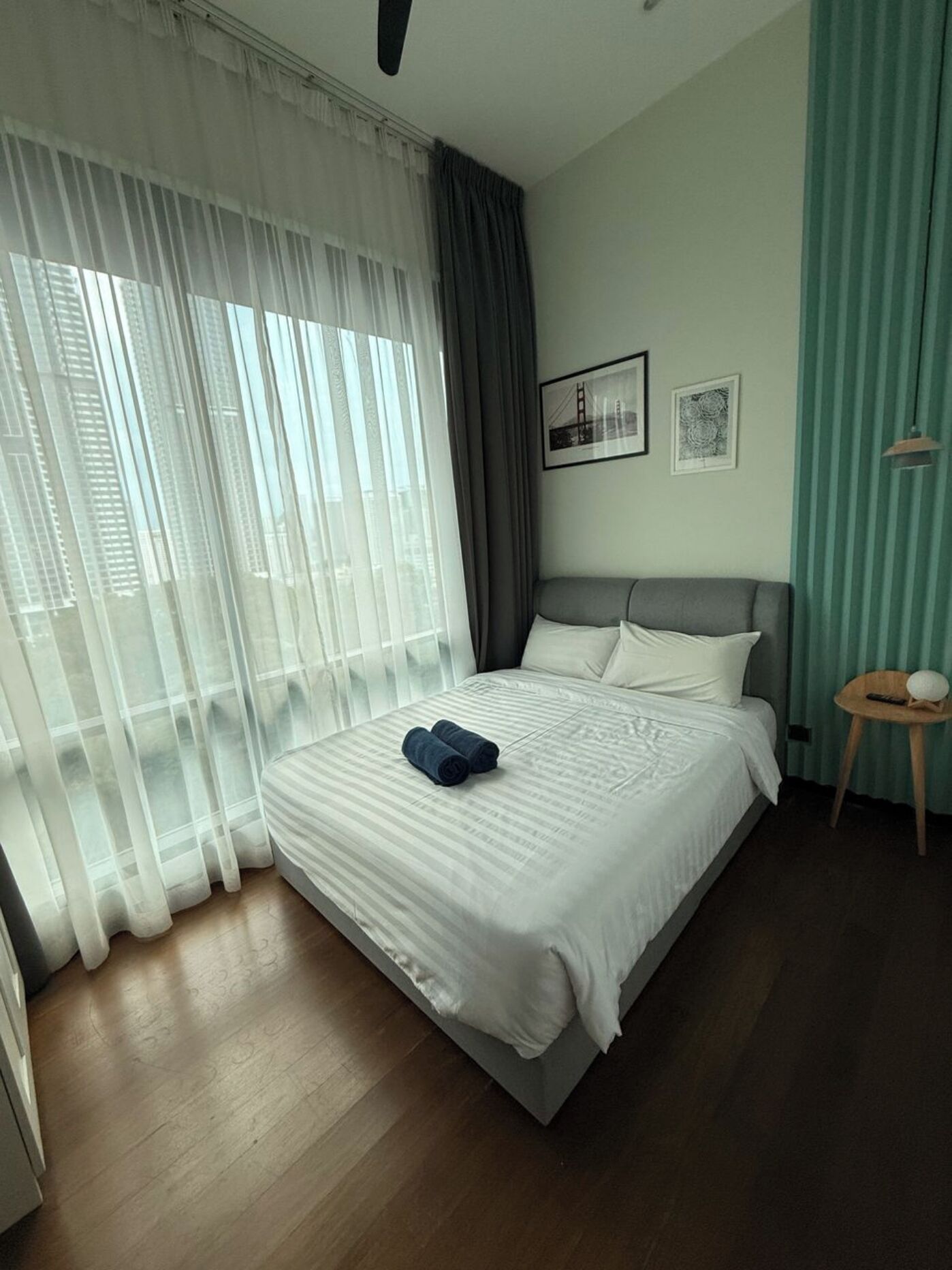 A hotel room with a large bed, a small round table with a lamp, and two framed pictures on the wall.