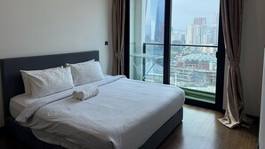 Een moderne hotelkamer met een groot bed, uitzicht op de stad door middel van kamerhoge ramen, en een gordijn aan de rechterkant.
