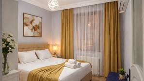 Una camera d'albergo con un letto grande, un comodino, una lampada, una finestra con tende e un tavolino con una pianta.
