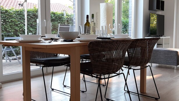A dining area with a wooden table, wicker chairs, and a television. - Vacation apartment Birkenhof Alfsee  (Rieste)