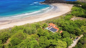 A coastal property with a beach view, solar panels, and lush greenery.