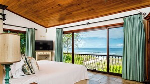 A bedroom with a large bed, a TV, and a view of the ocean.