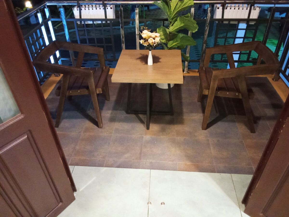 Un tavolo di legno con sedie e un vaso di fiori in una stanza con pavimento piastrellato e una ringhiera sullo sfondo.