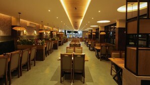 A spacious restaurant with wooden tables and chairs, a central walkway, and a modern ceiling design. - Holidays Garden Resort (Kalpetta)