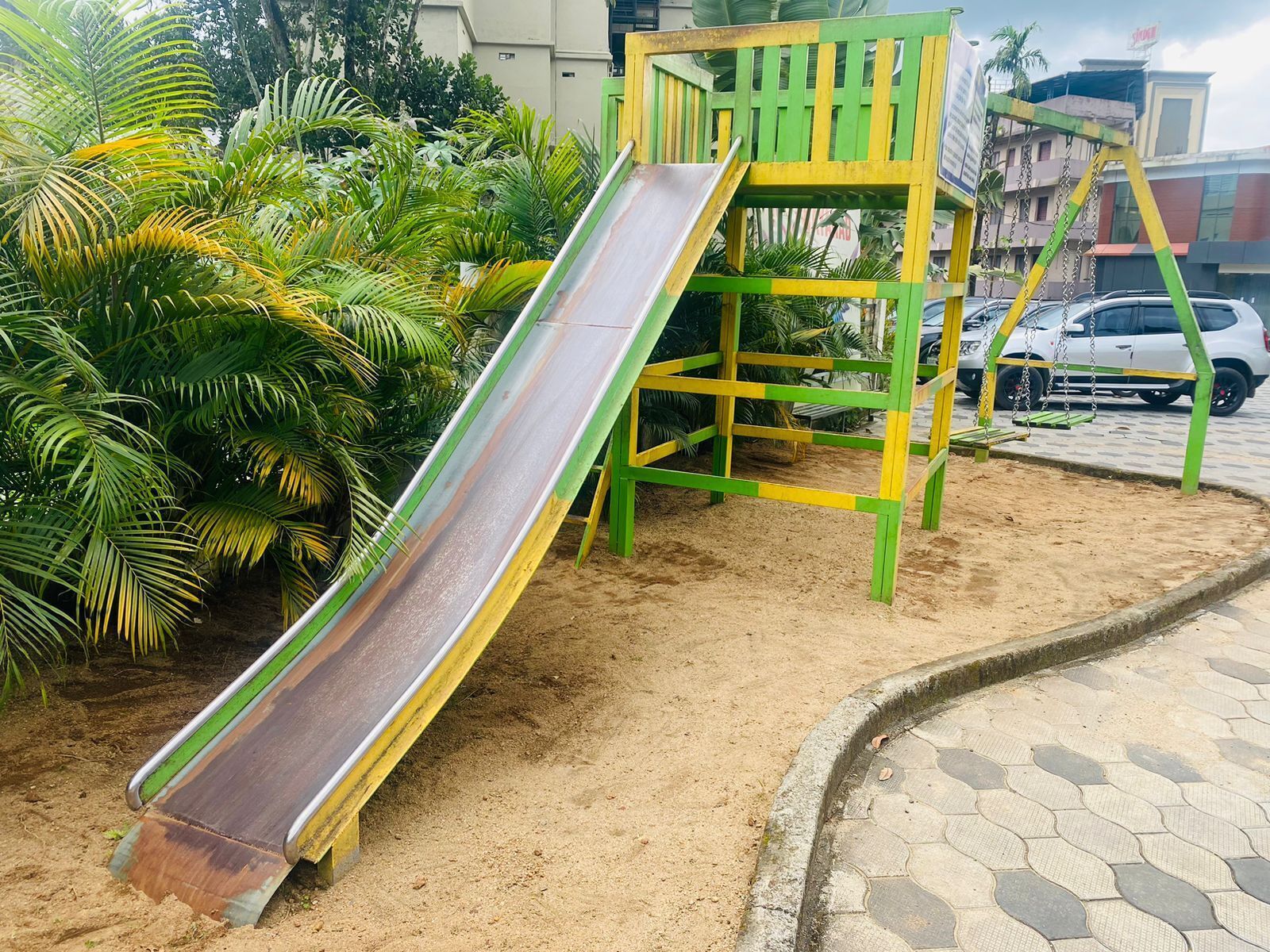 Un parque infantil con tobogán y estructura para escalar, rodeado de arena y palmeras.
