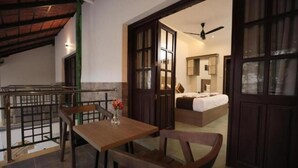 A room with a wooden table, a chair, a bed, and a ceiling fan. - Holidays Garden Resort (Kalpetta)