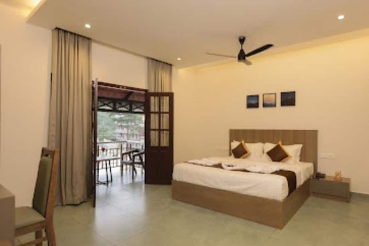 A hotel room with a bed, a ceiling fan, a small table, and a view of the outdoors.