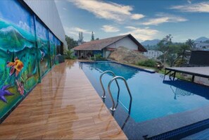 A swimming pool with a wooden deck and a mural of underwater scenery. - Holidays Garden Resort (Kalpetta)