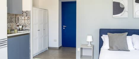 Un dormitorio con cama, mesita de noche y tocador. Hay una puerta azul que da a un baño.