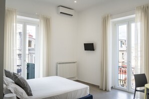 A hotel room with a bed, a TV, a radiator, and a view of the city through the window. - Duomo 5 - Maria s Bright Flat at the Cathed w Balc (Naples)