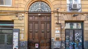 A brown double door with a decorative metal grille above it, set in a building with a stone facade. - Duomo 5 - Maria s Bright Flat at the Cathed w Balc (Naples)