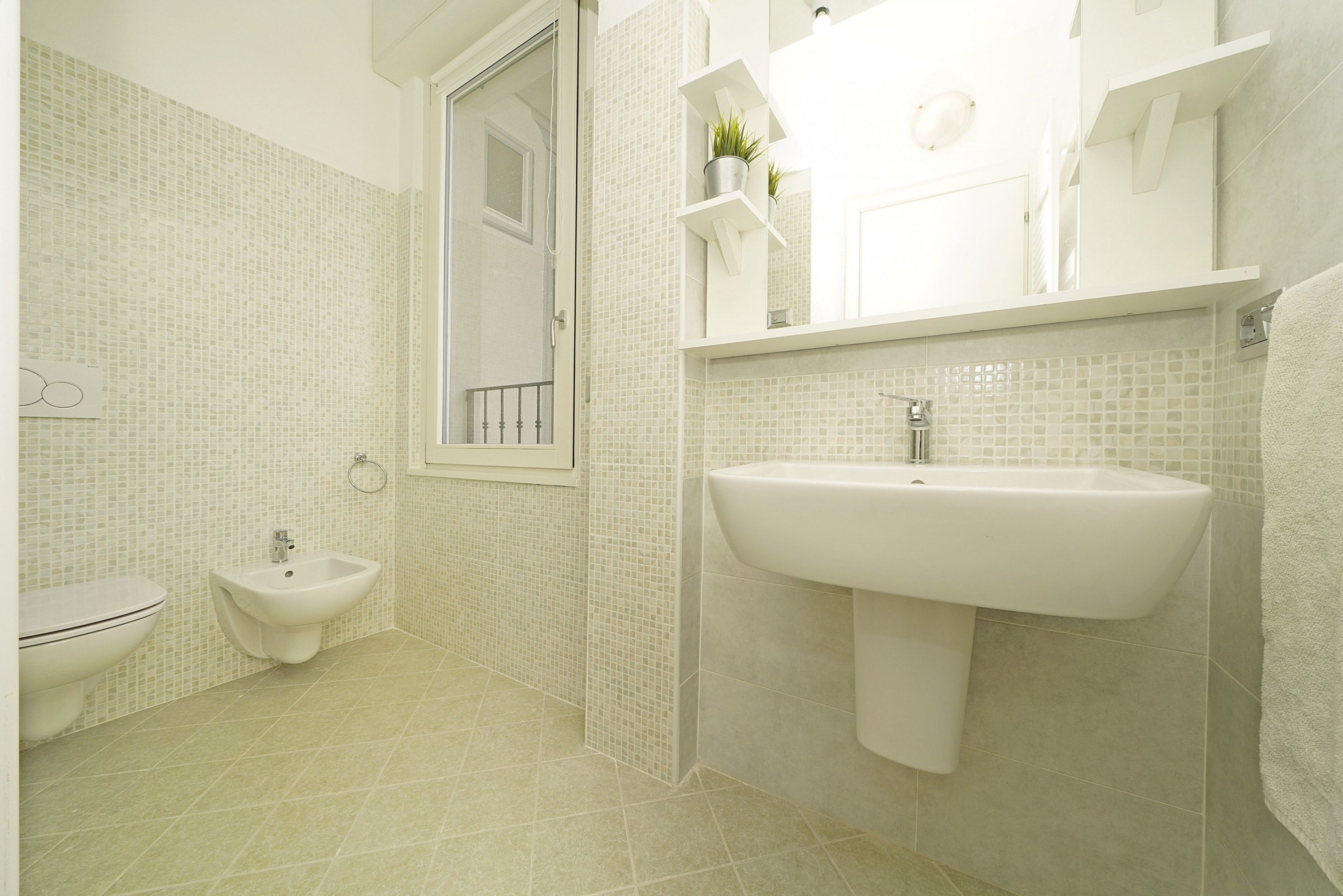 Et badeværelse med toilet, bidet, håndvask og flisebeklædte vægge.
