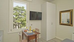 A dining area with a table set for two, a television mounted on the wall, and a window with a view of trees. - Villa Caterina 10 - LOC (Desenzano del Garda)