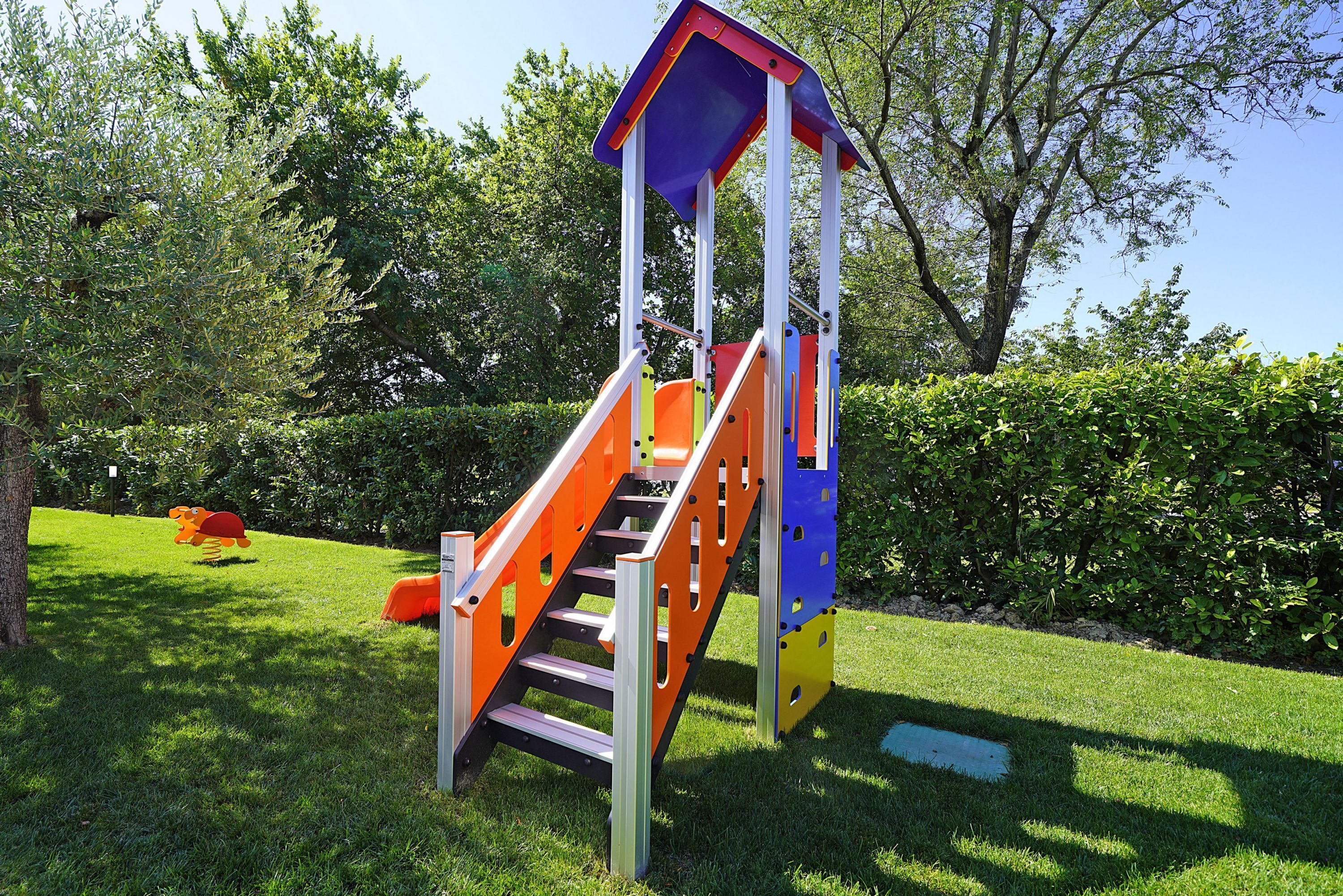A playground with a slide and climbing structure surrounded by grass and trees.