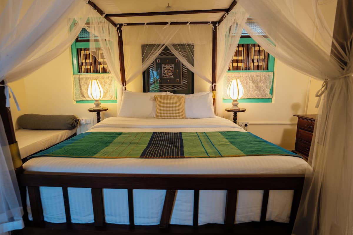 Una cama con dosel y cuatro columnas, dos lámparas de noche y vistas a un ventanal con diseño.