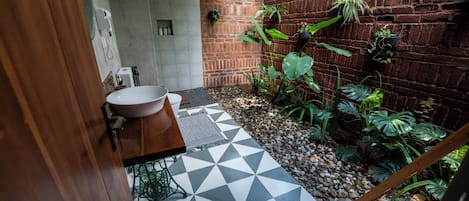 Un baño con lavamanos blanco, piso con estampado geométrico y pared de ladrillo con plantas en macetas.