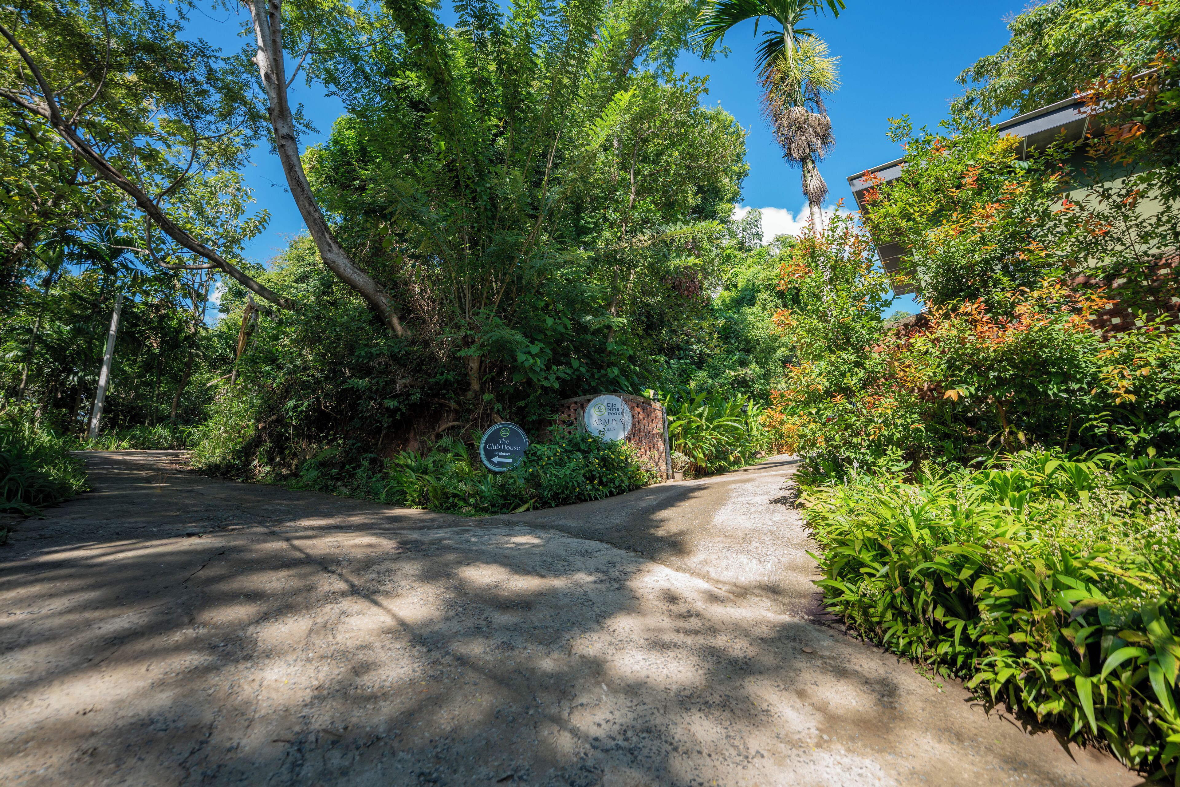 A paved pathway leading to a building with a sign indicating 'The Club House' and 'Ella Nine Peaks Villa'.