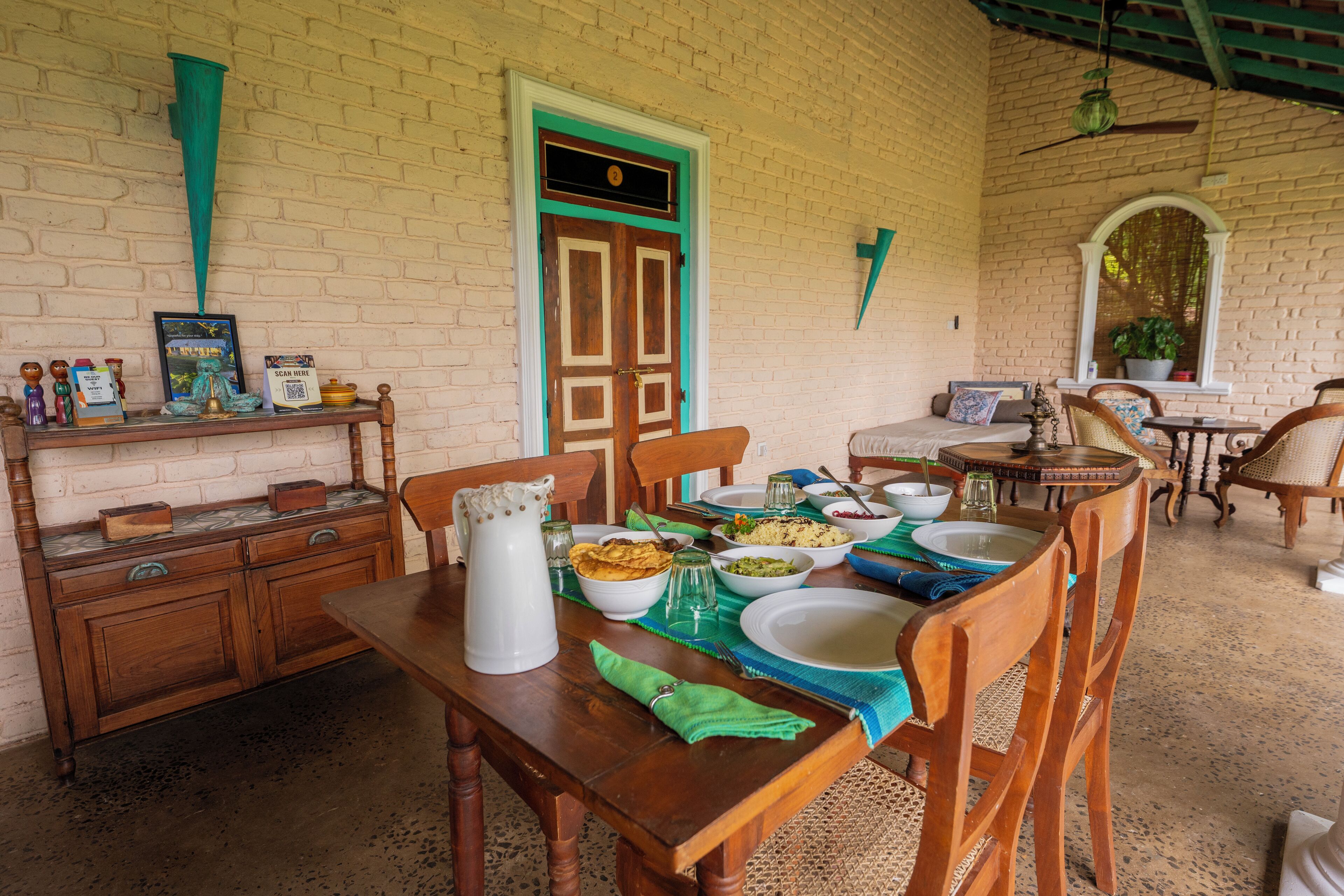 A dining area with a wooden table set for a meal, a bench, and a brick wall with a door.