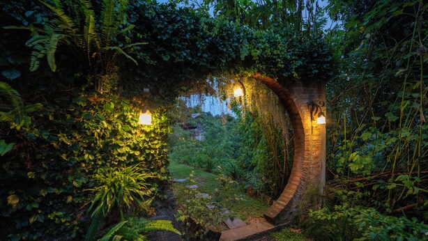 A brick archway with lights, surrounded by lush greenery and ferns.