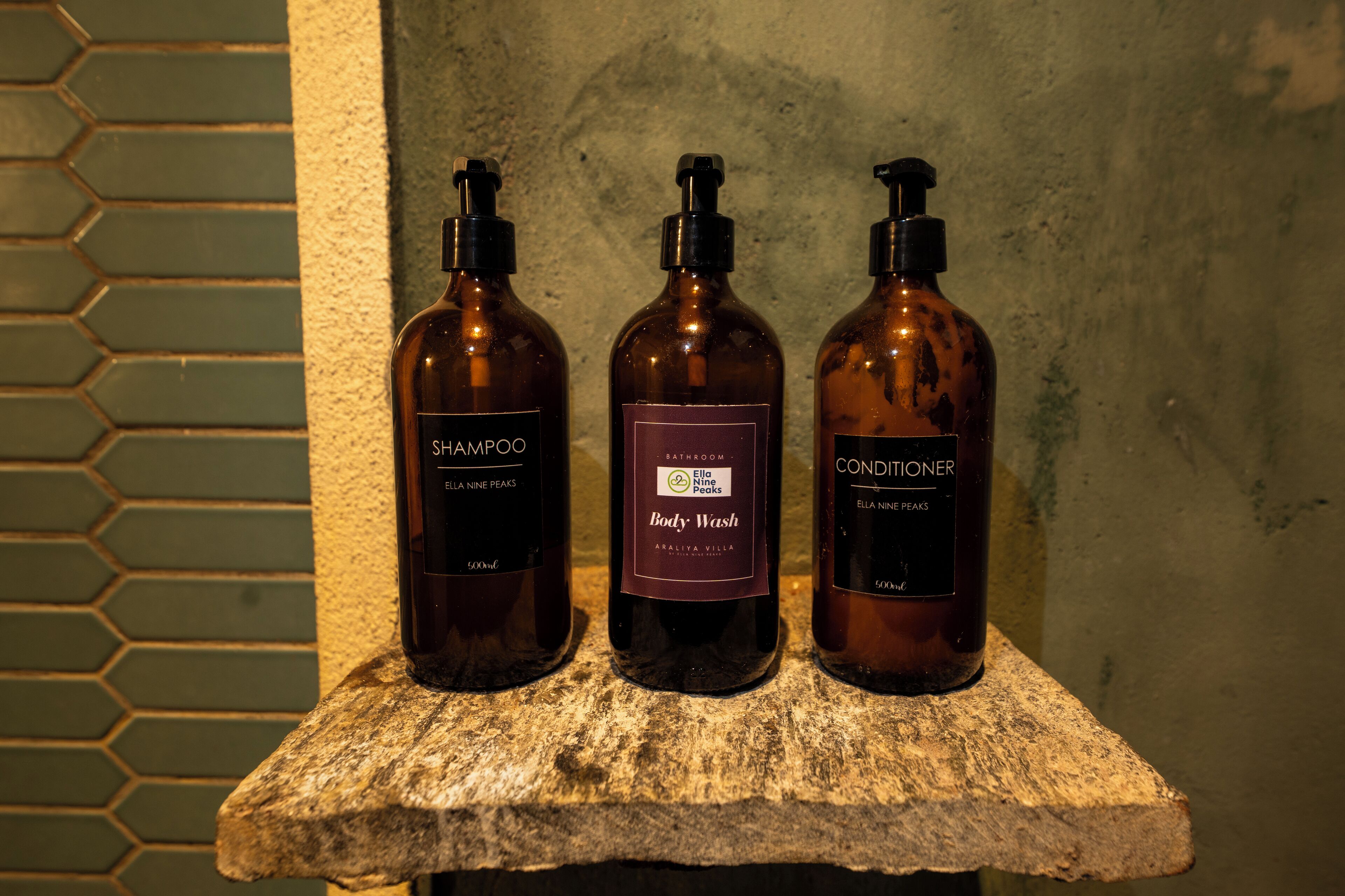 Three bottles of Ella Nine Peaks body wash and conditioner on a stone shelf.