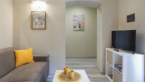 A living room with a sofa, a coffee table with two yellow mugs, a TV on a stand, and framed artwork on the walls. - Raibetta Apartments - Two (Genoa)
