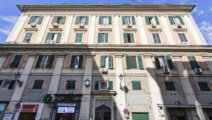 A multi-story building with a classic architectural style, featuring a central entrance with a decorative archway and a clock above it. - Raibetta Apartments - Two (Genoa)