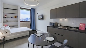 A compact hotel room with a bed, a dining table with cutlery, a TV, and a kitchen area with a microwave and sink. - Chic Modern Lofts - B - BK (Genoa)