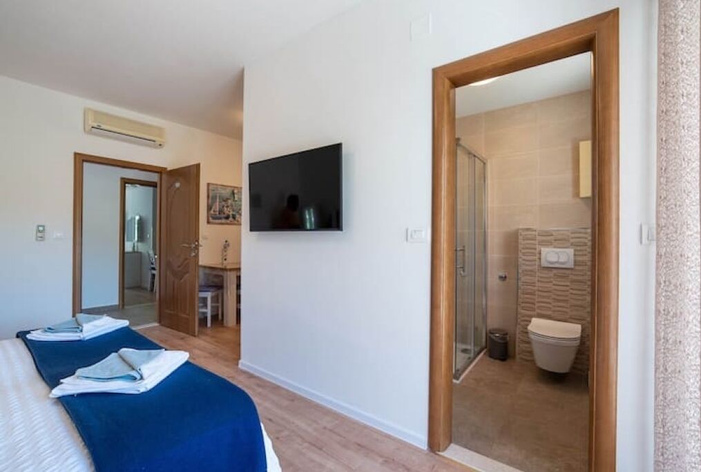 A hotel room with a bed, a TV, and a bathroom visible through an open door.