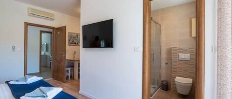 A hotel room with a bed, a TV, and a bathroom visible through an open door.