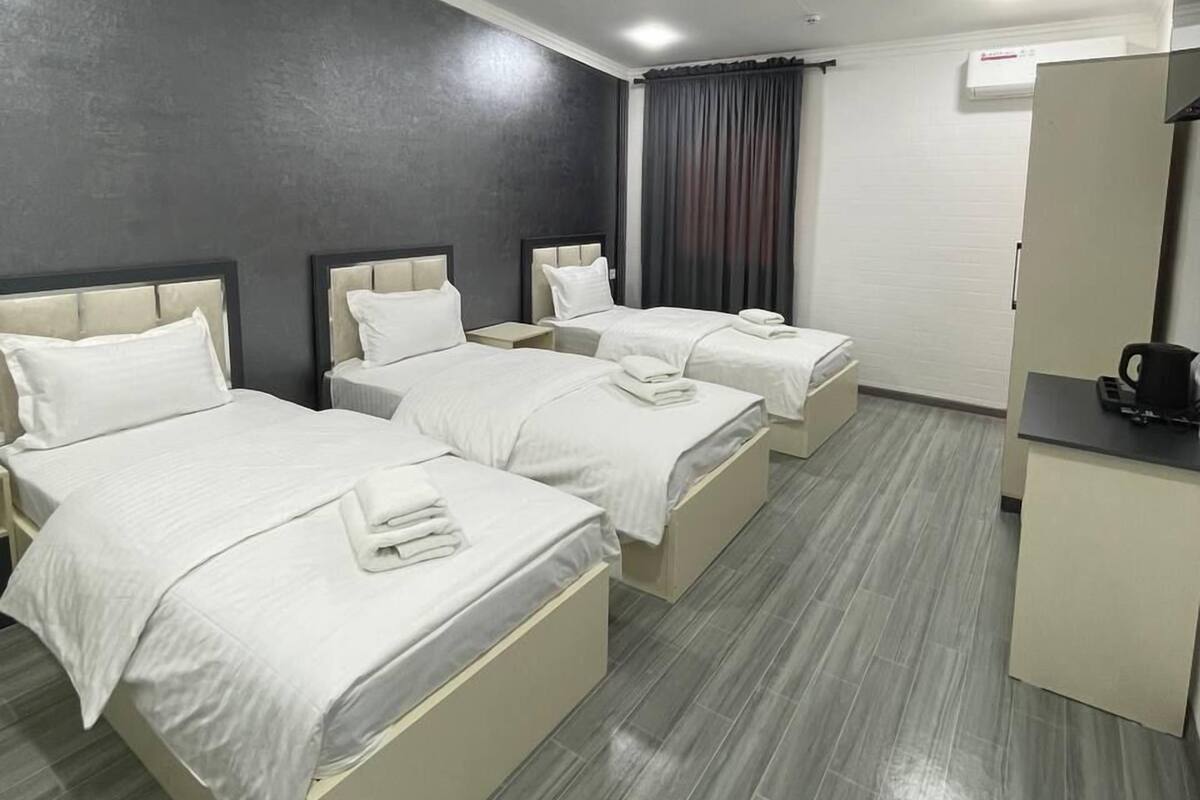 A hotel room with three beds, a desk, and a coffee machine.