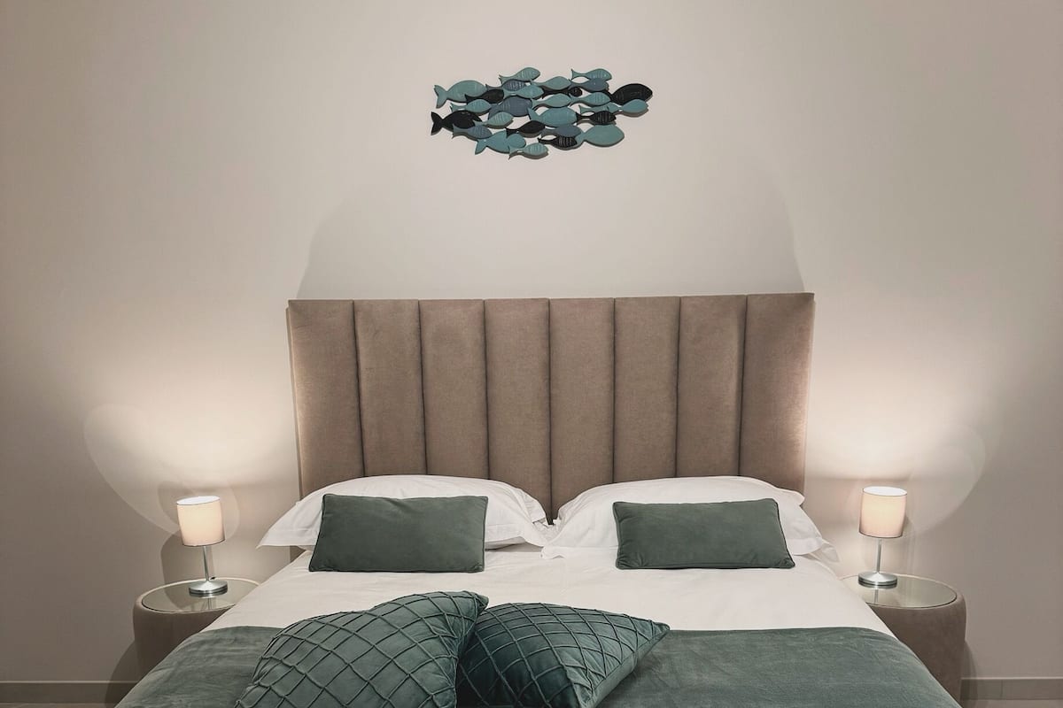 Un lit bien fait, avec une tête de lit, deux tables de chevet avec des lampes et un élément décoratif mural au-dessus du lit.