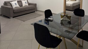 A modern living room with a glass dining table, black chairs, a grey sofa, and a large mirror. - Samarè Rooms & Apartments (Bisceglie)