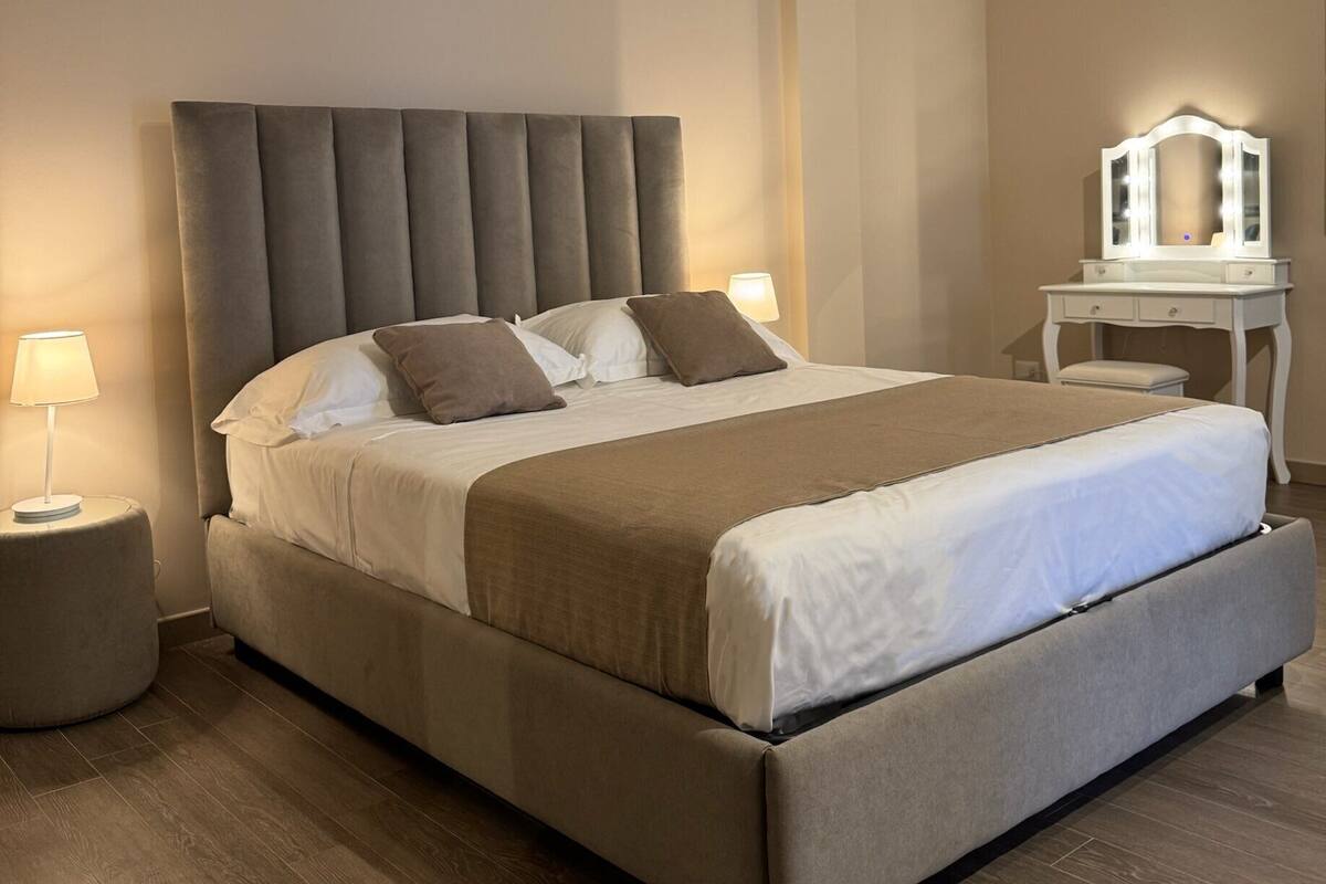 Une chambre moderne avec un grand lit, deux tables de chevet, une petite table et une coiffeuse avec un miroir.