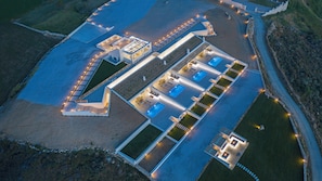 Ett flygbildsfoto av ett modernt semesterkomplex med flera pooler, en stor huvudbyggnad och ett väl upplyst utomhusområde.