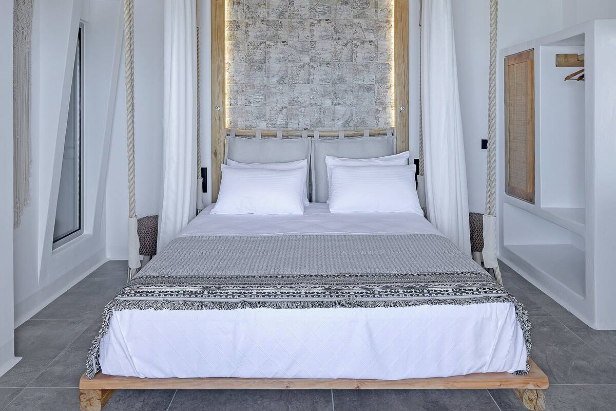 Een bed met houten frame en witte beddengoed, een stenen muur en zichtbare houten balken aan het plafond.