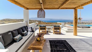 A wooden deck with a sofa, chairs, and a table with bowls. A hanging light fixture and a hanging plant are visible.
