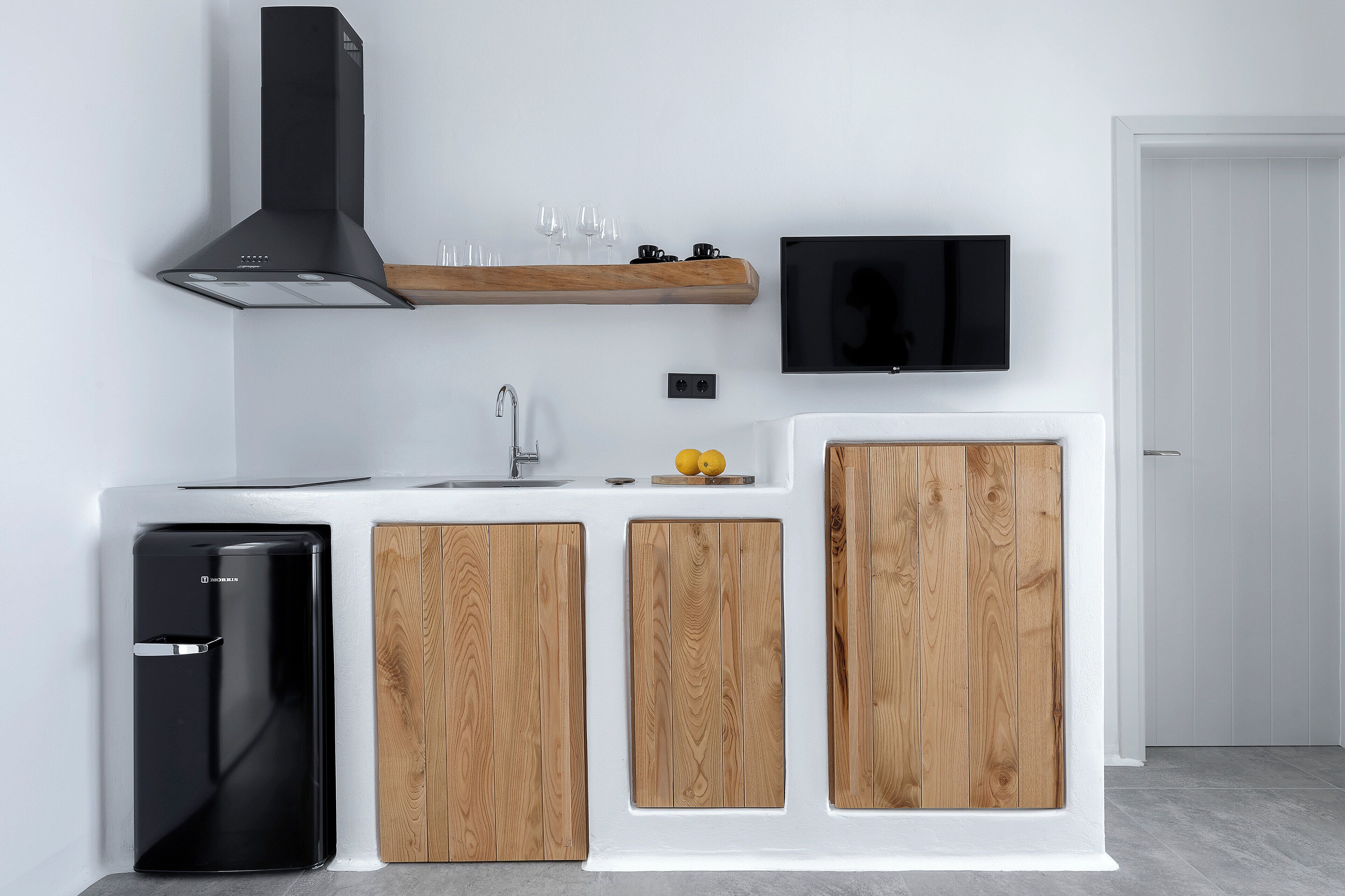 A modern kitchen with a black refrigerator, wooden cabinets, a built-in oven, a sink, and a mounted TV.