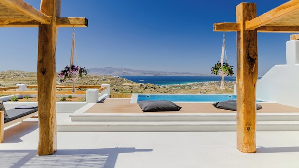 A wooden pergola with a hanging flower basket, a pool, and a view of the sea and mountains.