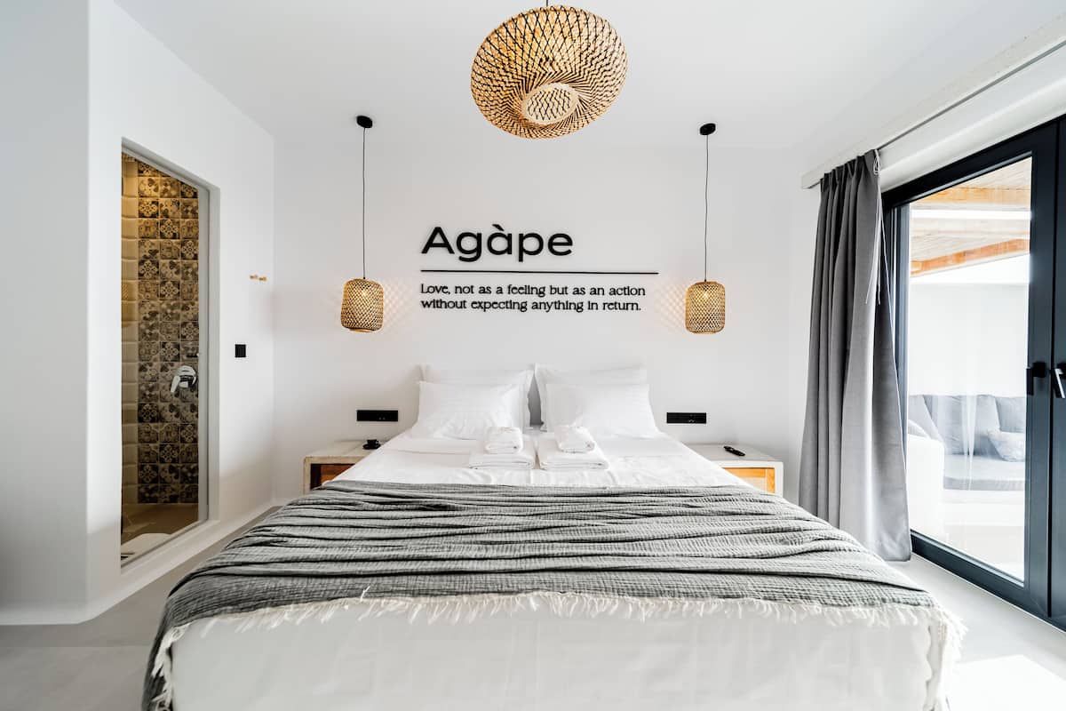 Een moderne hotelkamer met een groot bed, een decoratieve plafondlamp, uitzicht naar buiten en een muur met een citaat.