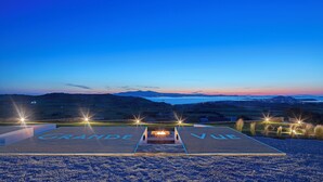 A parking area with "GRAND VUE" marked on the ground, surrounded by a scenic landscape with mountains and a body of water in the distance.