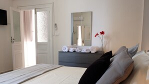 A hotel room with a bed, a dresser with towels, a mirror, a TV mounted on the wall, and a door with a curtain.