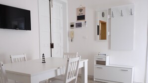 A white room with a TV, a door, a coat rack, a small table with a lamp, and a cabinet.