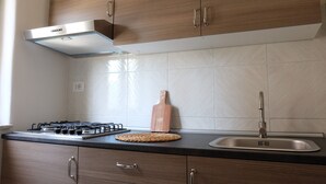 A modern kitchen with wooden cabinets, a gas stove, a stainless steel sink, and a woven cutting board.
