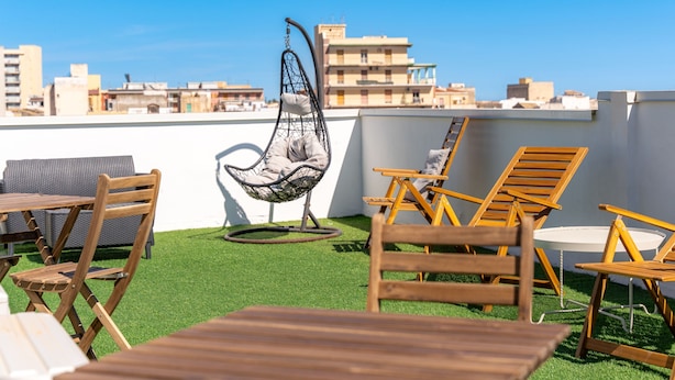 A rooftop terrace with wooden furniture, a hanging chair, and a view of city buildings. - Myia 1A in Siracusa With 1 Bedrooms and 1 Bathrooms (Syracuse)
