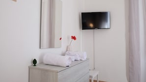 A hotel room with a wooden dresser, a flat-screen TV mounted on the wall, a mirror, and a small potted plant. - Myia 1A in Siracusa With 1 Bedrooms and 1 Bathrooms (Syracuse)
