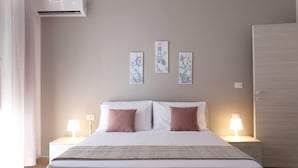 A hotel room with a bed, two bedside lamps, a wall-mounted air conditioner, and three framed nautical-themed pictures. - Myia 1A in Siracusa With 1 Bedrooms and 1 Bathrooms (Syracuse)