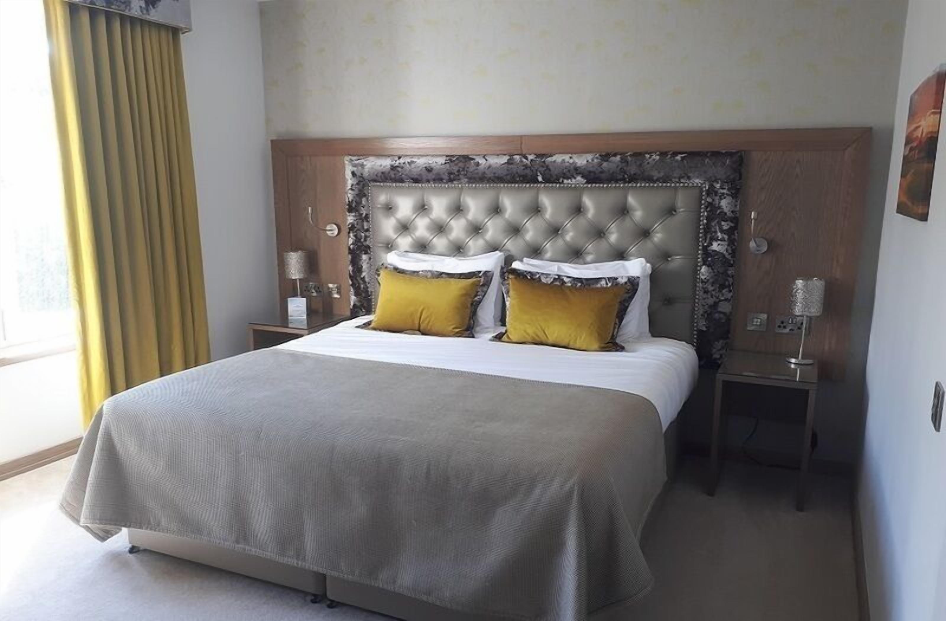A hotel room with a large bed, a wooden headboard, two bedside tables, and a window with curtains.